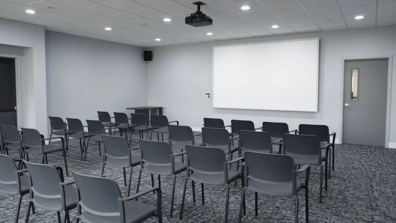 An empty seminar room with a blank projector screen and chairs in rows, and no people, logos, or readable slides.